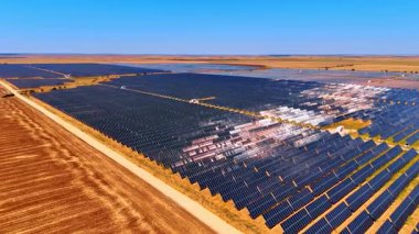 Manzara boyunca güneş panelleri. Büyük bir güneş çiftliği, kırsal bir alanda açık mavi gökyüzünün altında güneş ışığını emen sıra sıra güneş panellerini sergiliyor..