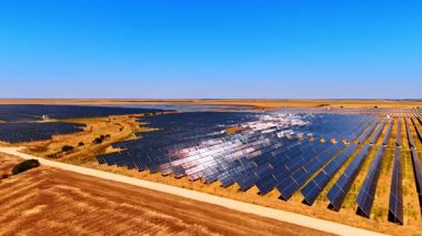 Açık gökyüzünün altındaki güneş çiftliği manzarası. Geniş güneş panelleri kuru bir araziyi kaplayarak güneşli ve bulutsuz bir ortamda yenilenebilir enerji üretir..