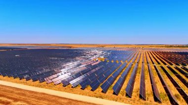 Kırsal bölgede geniş bir güneş enerjisi çiftliği. Güneş panelleri açık mavi gökyüzünün altında kırsal bir araziye yayılarak, yenilenebilir enerjiyi iş başında vurguluyor.