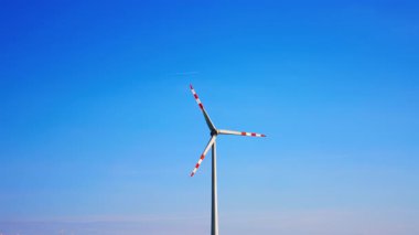 Rüzgar değirmeninin dönen bıçaklarında beyaz ve kırmızı çizgiler. Arkaplanda açık mavi gökyüzü.