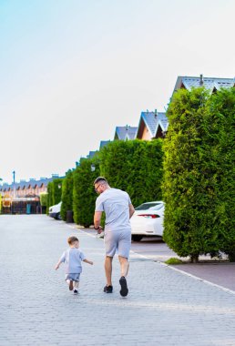 Baba ve çocuk eve yürüyor. Bir baba, evlerinin ve ağaçlarının olduğu sessiz bir banliyö sokağında, küçük çocuğunun yanında neşeyle koşar..