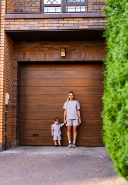 Anne ve çocuk garaj kapısında bekliyor. Bir anne ve çocuğu, ahşap bir garaj kapısının yanında eşleşen kıyafetlerle poz veriyorlar..