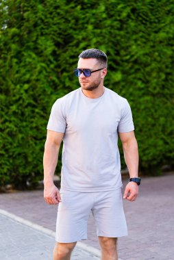 Gündelik kıyafetli adam güneşten hoşlanır. Açık renk giyinmiş bir adam yemyeşil bir yolda kendine güvenerek duruyor..