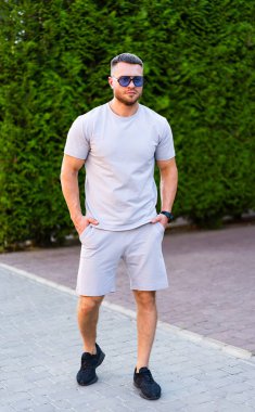 Yazlık kıyafetlerle yürüyen bir adam. Güneşli bir günde, yeşil bir giysi içinde, kaldırımlı bir yolda gelişigüzel yürüyen bir adam..