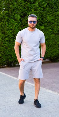 Kendine güveni olan bir adam yaz kıyafetiyle dolaşıyor. Gündüz vakti yeşil çitlerle çevrili bir patika boyunca günlük kıyafetli bir adam yürüyor..