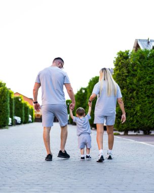 Güneşli bir günde şortla aile gezintisi. Bir aile, aynı kıyafetleri giyerek, güneşli bir günün tadını çıkarırken, ağaçlarla kaplı bir patikada el ele yürür..