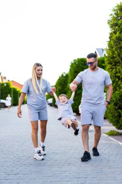 Aile, parkta güneşli bir günün tadını çıkarır. Güneşli bir günde bir aile birlikte dolaşır, elleri ele tutuşur, oğulları sevinçle aralarında sallanırken..