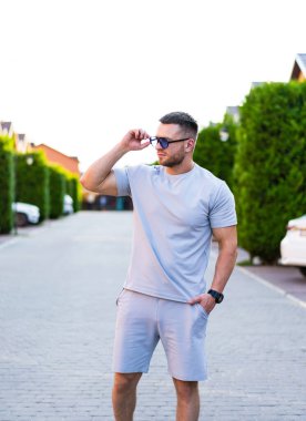 Yazın tadını çıkaran bir adam. Güneşli bir günde güneş gözlüğünü düzeltirken günlük kıyafetlerini giymiş bir adam kendine güveniyor..