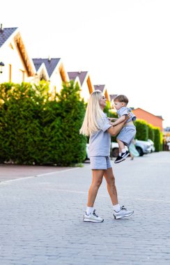 Anne ve çocuk akşam yürüyüşünde. Bir anne, akşam ışığında huzurlu bir sokakta yürürken küçük çocuğunu kucağına alır..