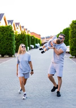 Aile gezintisi güneşte. Bir aile kaldırımlı bir caddede yürüyor, birlikte vakit geçiriyorlar..