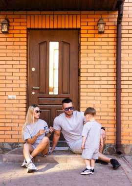 Aile dışarıda eğleniyor. Bir aile evinin merdivenlerinde oturur, güneşli bir günün tadını çıkarırken çocuğuyla mutlu bir şekilde iletişim kurar..