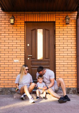 Aile, eşikte birlikte vakit geçirmekten hoşlanır. Üç kişilik bir aile, tuğla evlerinin kapısında rahatlar, neşeli anları ve kahkahaları paylaşır..