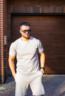 Şık bir adam dışarıda poz veriyor. İyi giyimli bir adam, güneşli bir günde modern bir binanın dışında güneş gözlükleriyle güvenle durur..