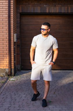 Şık bir adam sokakta öylesine yürür. Yaz kıyafetleri içinde bir adam, sıcak güneş ışığı altındaki bir garajın yakınındaki kaldırım taşı patikasında yürüyor..