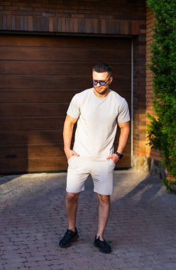 Açık havada yazın tadını çıkaran şık bir adam. Güneşli bir günde, açık renkli bir elbise ve güneş gözlüğü takan bir adam kendine güvenerek bir yürüyüş yolunda durur..