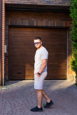 Garajın yanında yürüyen şık bir adam. Günlük kıyafet giyen bir adam güneşli bir günde garajın dışındaki patikada güven içinde dolaşır..