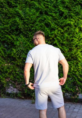 Yeşil elbiseli bir adam. Gündelik kıyafetli bir adam, sırtı kameraya dönük, güneşin altında, yoğun yeşil bir çalılıkta dikiliyor..