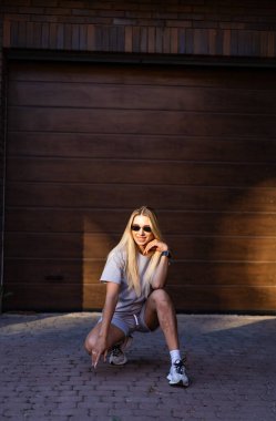 Garajda kendine güvenen genç bir kadın. Genç bir kadın güneşli bir günde garajın önünde neşeli bir şekilde poz verir. Havası ve kendine güveni vardır..