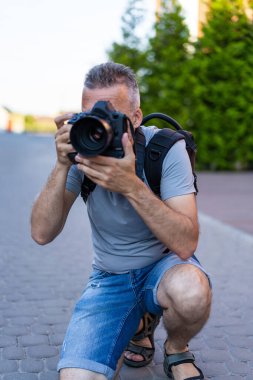 Şehir fotoğrafçısı iş başında. Bir fotoğrafçı şehir ortamında çömelmiş, kamerasına odaklanarak caddede anları çekmeye hazırlanıyor..