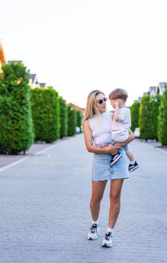 Güneşli bir günde hamile bir anne. Bir kadın parlak, güneşli bir günde ağaçlarla kaplı bir yolda yürürken küçük oğlunu kucağına alır..