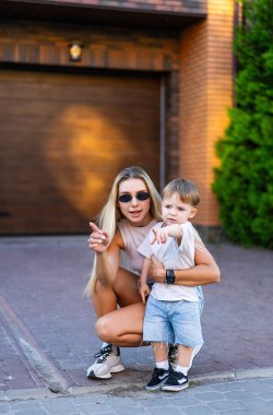 Anne ve oğlu güneşte. Bir anne, sıcak güneş ışığında evinin önünde genç oğlunun yanında diz çökerken şakacı bir şekilde işaret eder..