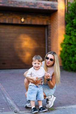 Günbatımı aile zamanı dışarıda. Bir kadın ve genç bir çocuk gün batımında evlerinin önünde neşeli bir anın tadını çıkarıyorlar, gülümsüyorlar ve oynuyorlar..