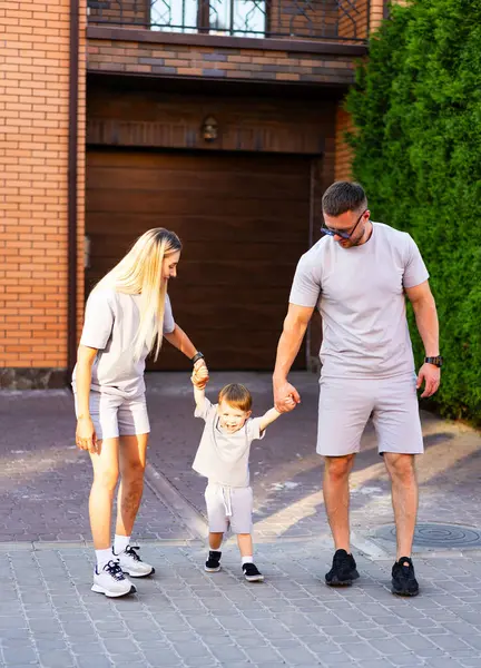 Yazın dışarıda aile eğlencesi. Mutlu bir aile sokakta yürüyor, el ele tutuşuyor ve güneşli bir yaz gününde kahkahalarını paylaşıyor..