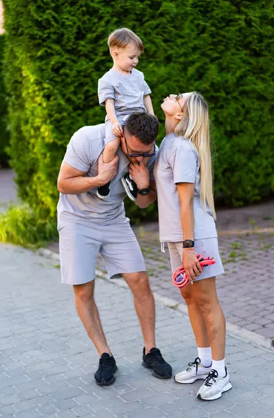 Dışarıda neşeli bir aile var. Bir aile, yeşil bir parkta birlikte oynuyor. Yanında bir çocuk, babasının omuzlarında ve annesi gülümsüyor..