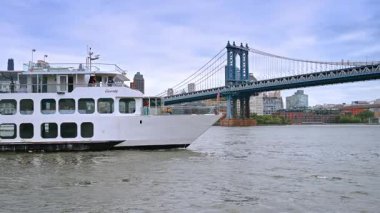 Beyaz çoklu güverte teknesi nehir manzarasında yavaşça ilerliyor. Araç gri bir günde Manhattan Köprüsü 'ne yaklaşıyor..
