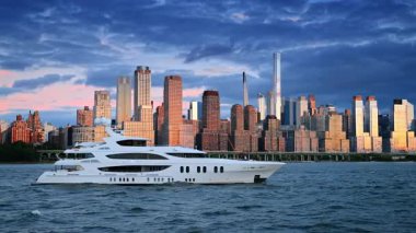 Çalkantılı nehir manzarasında güzel, modern bir yat. Manhattan silueti rıhtımda batan güneşin ışığında. Arkaplanda koyu mavi bulutlar.