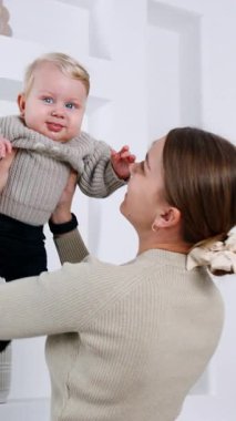 Genç anne tatlı bebeğini kucağında tutuyor. Gri kazaklı anne ve bebek portresi. Dikey video