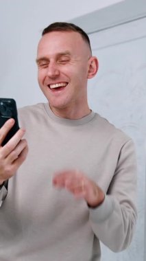 Beyaz bir erkek telefonuna bakıyor. Odada duran bir alet kullanan adam. Dikey video