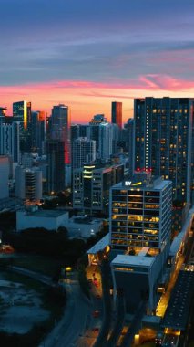 Miami, Florida 'nın göz kamaştırıcı binalarının üstündeki insansız hava aracı görüntüleri. Metropolün alacakaranlıktaki manzarası. Dikey video