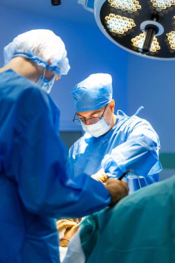 Bir grup cerrah hastane tiyatrosunda ameliyat yapıyor. Ameliyat sırasında steril giysili doktorlar birlikte çalışıyorlar..