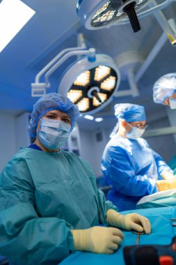 Ameliyat sırasında steril önlüklü kadın cerrah. Koruyucu önlüklü ve eldivenli bir kadın cerrahi operasyon sırasında kameraya bakıyor..