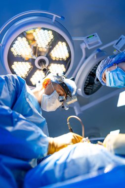Cerrah, parlak cerrahi ışıklar altında ameliyat yapıyor. Modern bir ameliyathanede tam donanımlı tıbbi uzman ameliyat yapıyor..