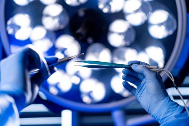 Cerrahlar ameliyathanede cerrahi aletleri tutuyorlar. Cerrahların ellerinin parlak ameliyat ışıkları altında cerrahi aletleri tutarken yakın plan çekimleri..