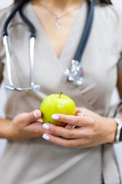 Doktor steteskopla elma tutuyor. Tıbbi uzman steteskop takarken yeşil elma tutuyor. Sağlıklı yaşam tarzını ve beslenmeyi simgeliyor..