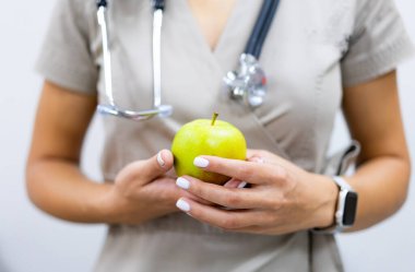 Doktor elma tutuyor. Sağlık sembolü olarak taze yeşil bir elma tutan bir doktorun yakın çekimi ve düzgün beslenme.