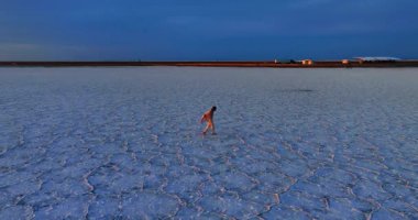 Beyaz ceketli Afro-Amerikalı adam, Utah, ABD 'deki Bonneville Tuz Düzlükleri' nin tuzlu kabuğunun yanından geçiyor. Arka planda batan güzel güneş ve dağ siluetleri. Hava görünümü.