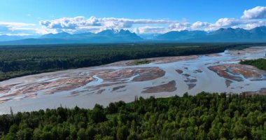 Delta nehrinin çevresinde yemyeşil ormanlar yetişir. Pofuduk bulutların altındaki görkemli dağlar. Alaska, ABD 'nin doğasına hava perspektifi.