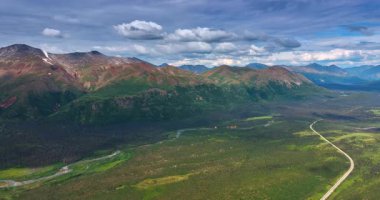 Muhteşem dağlar ve ayağındaki yeşil vadi. Bir otoyol ve dar bir nehir manzarayı geçer. Hava görüntüsü. Alaska, ABD.