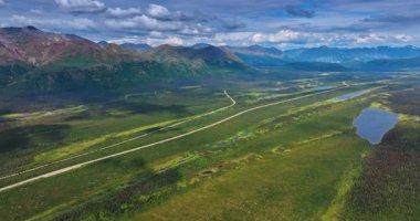 Alaska, ABD 'nin vahşi doğasının fantastik manzarası. Uçsuz bucaksız yeşil vadinin üstündeki insansız hava aracı görüntüleri nehirler ve otoyollarla kesişiyor ve sıradağlar tarafından özetleniyor..