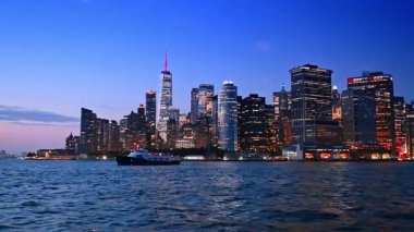 Tekne, alacakaranlıkta yırtık pırtık su manzarası boyunca seyahat eder. Arka planda New York 'un muhteşem silueti.