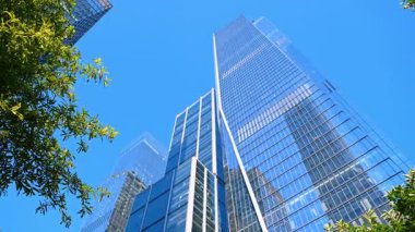 New York 'un modern cam binaları güzel mavi gökyüzünü yansıtıyor. Metropolis sokaklarında yürüyen yüksek binaların alçak açılı görüntüsü.