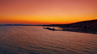 Altından gökyüzü ve suyun üzerindeki yansımalarıyla denizin üzerinde parlak bir gün batımı. Durgun denizin üzerine yansıyan altın ve turuncu tonlarıyla renkli bir günbatımı manzarası..