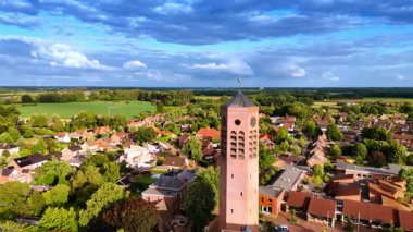 Yüksek tuğlalı kilise kulesi olan Hollanda şehrinin havadan görünüşü. Evler ve yeşil tarlalarla çevrili yüksek tuğlalı bir kilise kulesi olan Hollanda şehrinin insansız hava aracı görüntüsü..