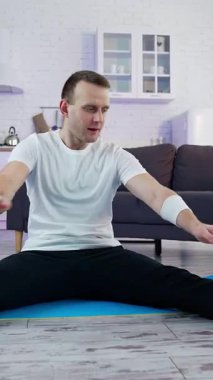 Genç atletik sağlıklı erkek içeride antrenman yapıyor. Karantinadaki güçlü adam evde çalışıyor. Dikey video