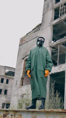 Mahvolmuş şehirde koruyucu giysili biri duruyor. Biyolojik tehlike kıyafeti giymiş bir adam. Dikey video