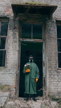 Bitkili biyo-tehlike kıyafeti giyen bir adam. Mahvolmuş şehirde koruyucu giysili biri duruyor. Dikey video